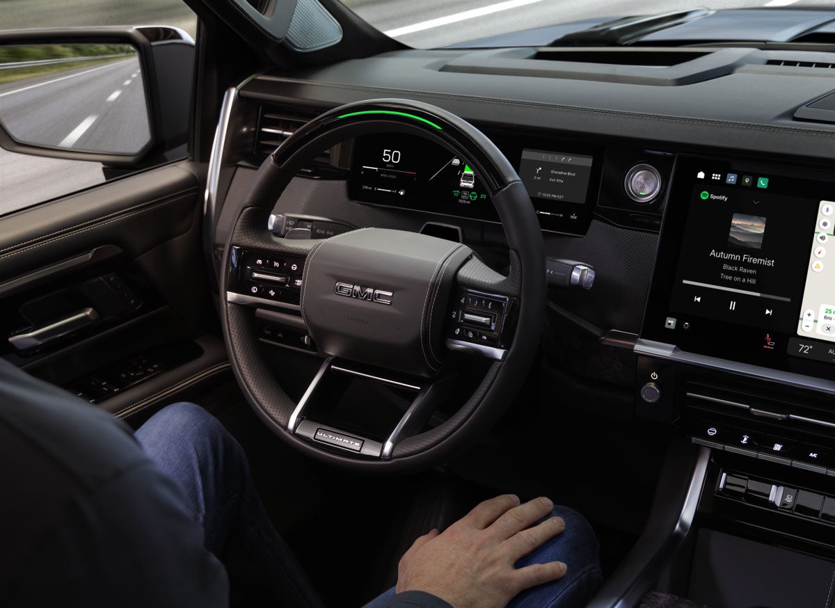 Driver's perspective of a GMC interior, showcasing the steering wheel, digital dashboard, and infotainment screen.